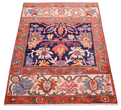 Antique floral area rug shown at an angle, featuring navy, orange, and cream with floral panels.