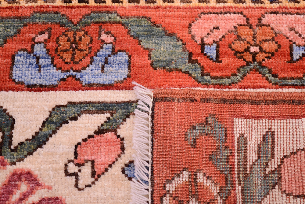 Close-up edge of antique floral rug with fringe, orange and cream fields, and woven pattern.