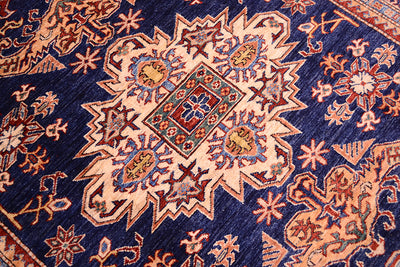 A close-up of a traditional patterned fine Afghan Kazak rug featuring a navy blue field with a large central medallion in beige, rust red, and blue.