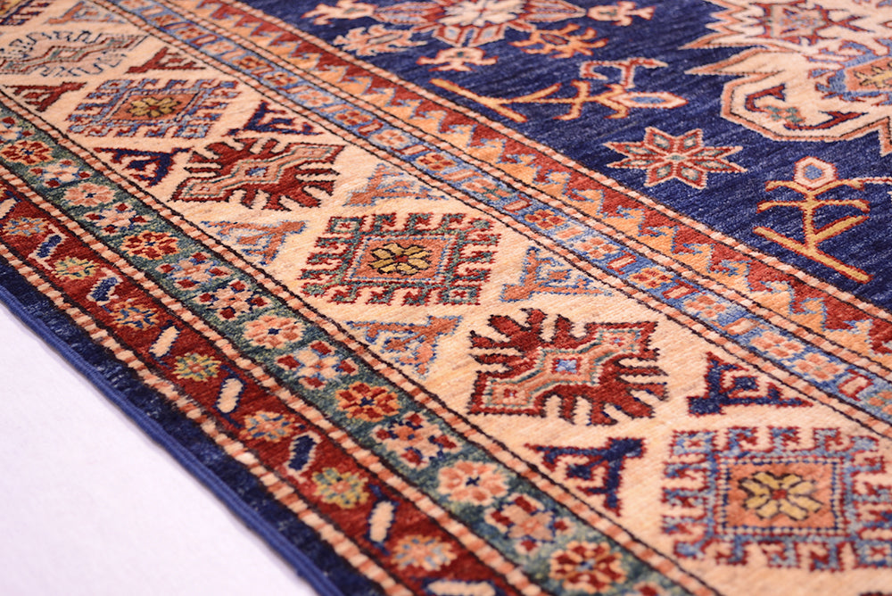 A close-up of a traditional patterned rug with a navy blue field, beige borders, and red, orange, and blue geometric motifs.