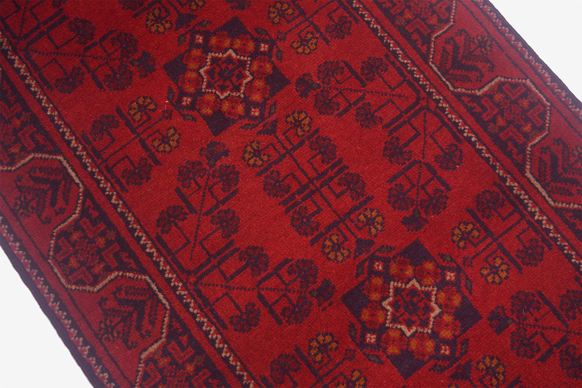 A close-up of a red patterned Afghan  rug with dark navy and brown geometric motifs and borders.
