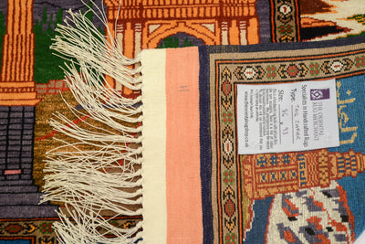 Close-up of a Fine Pictorial Afghan rug corner showing cream fringe, a peach stripe, a white product label, and a multicoloured geometric patterned field.