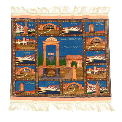 A hand-knotted Fine Pictorial Afghan rug wool and silk pile featuring a grid of architectural scenes from Afghanistan, including arches, mountains, and minarets, with cream fringe on the top and bottom. The centre panel reads 'Made by Meyza Hosain TAQ ZAFAR'.